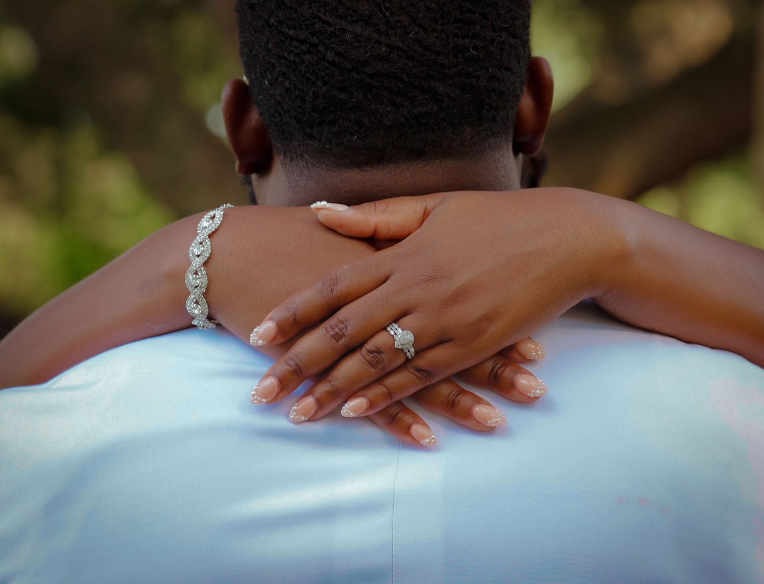Close-up of a bride's hand with diamond engagement ring and bracelet resting on groom's shoulder.