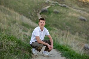 Senior Pictures guy crouching on dirt path in the hills milestones portraits