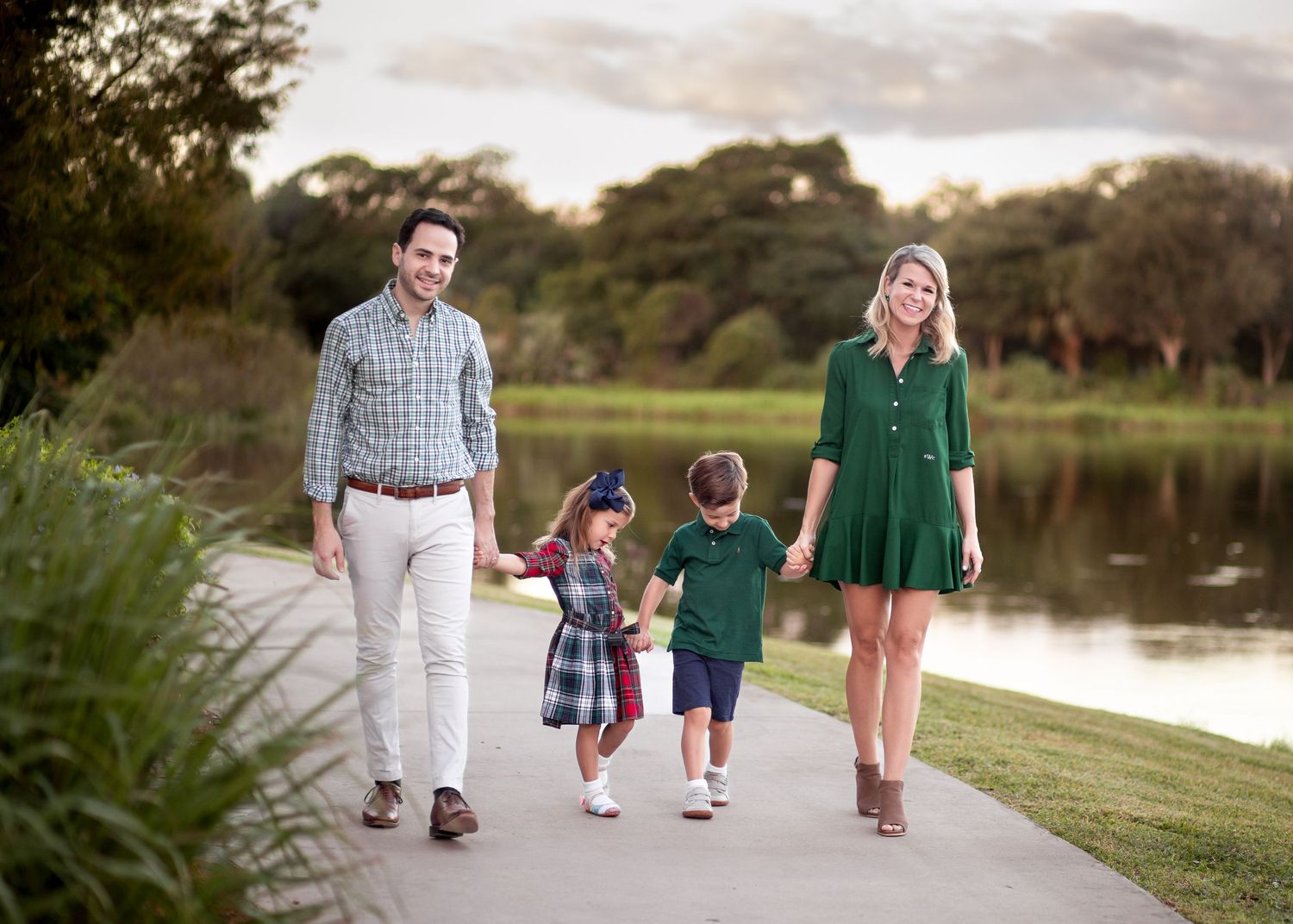 Family of four walking hand-in-hand on a scenic park path near a pond at sunset. Pondhawk Natural Area Park in Boca Raton.