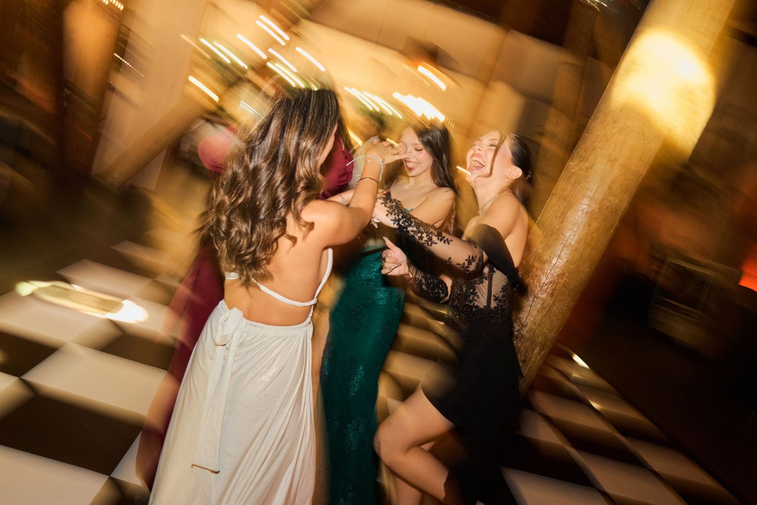 A group of people dancing and celebrating at an evening wedding reception in a warmly lit venue.
