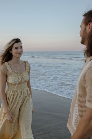 Two people in light colored clothing walk along a misty beach at sunset with ocean waves in the background.