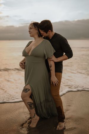 A couple embraces tenderly on a sandy beach at sunset, creating an intimate silhouette against the warm sky.