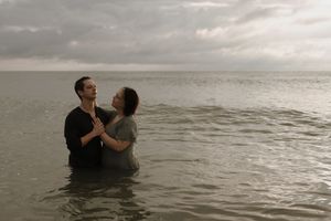 A couple embraces while standing in the ocean water at sunset, creating a romantic silhouette against the horizon.