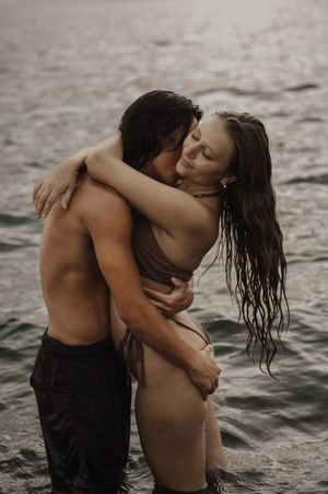 A couple embraces intimately in shallow water during an atmospheric photo session at dusk.
