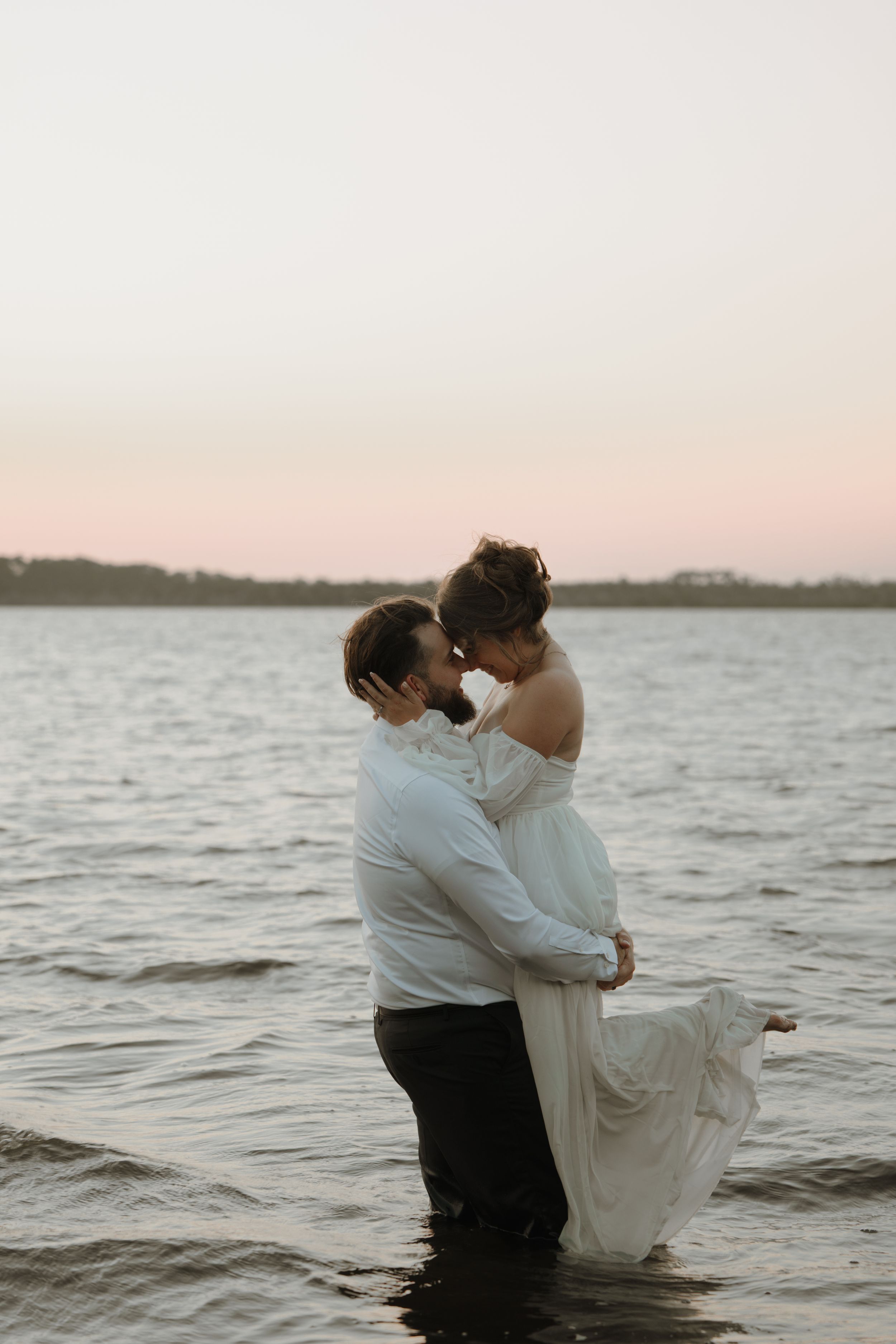 A romantic couple embraces while standing in shallow ocean waters at dusk, creating dreamy  photos along Florida's beautiful Ormond Beach.