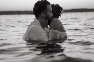 A romantic couple embraces while standing in ocean water at sunset creating a series of silhouetted poses.