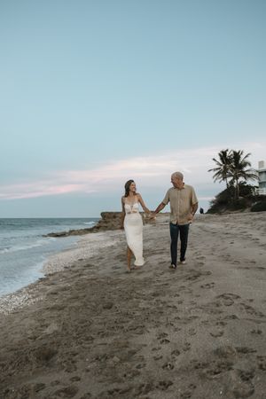 A couple walking hand in hand along a serene beach at sunset with palm trees in the background in Stuart, Florida at golden hour.