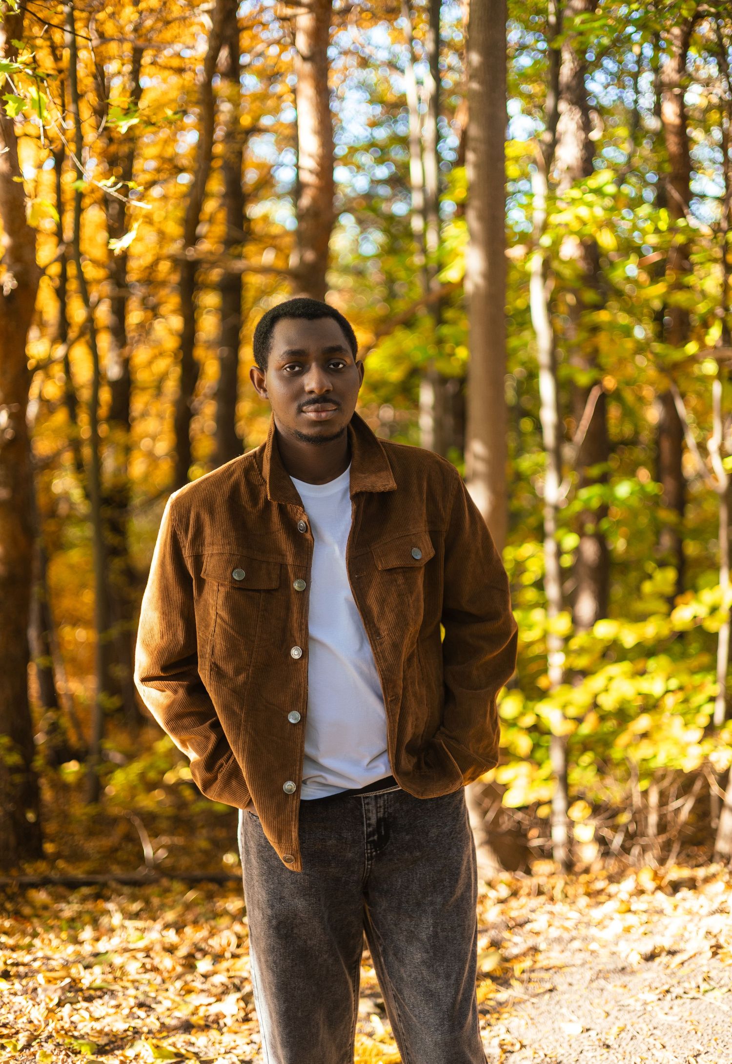 Young Black man in brown suede jacket posing in colorful autumn forest with golden foliage background.