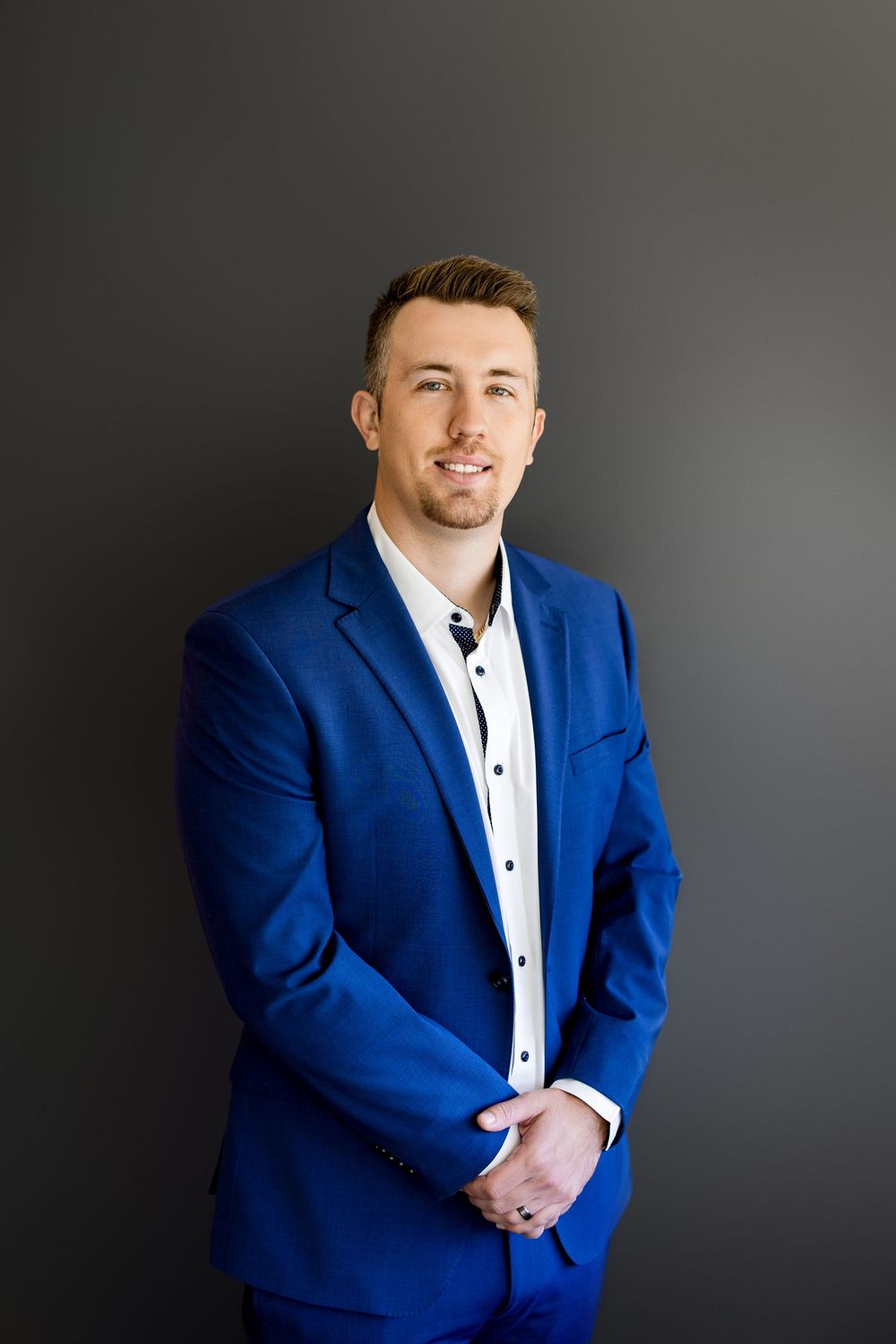 Professional man in blue suit smiling confidently against dark background for business headshot.