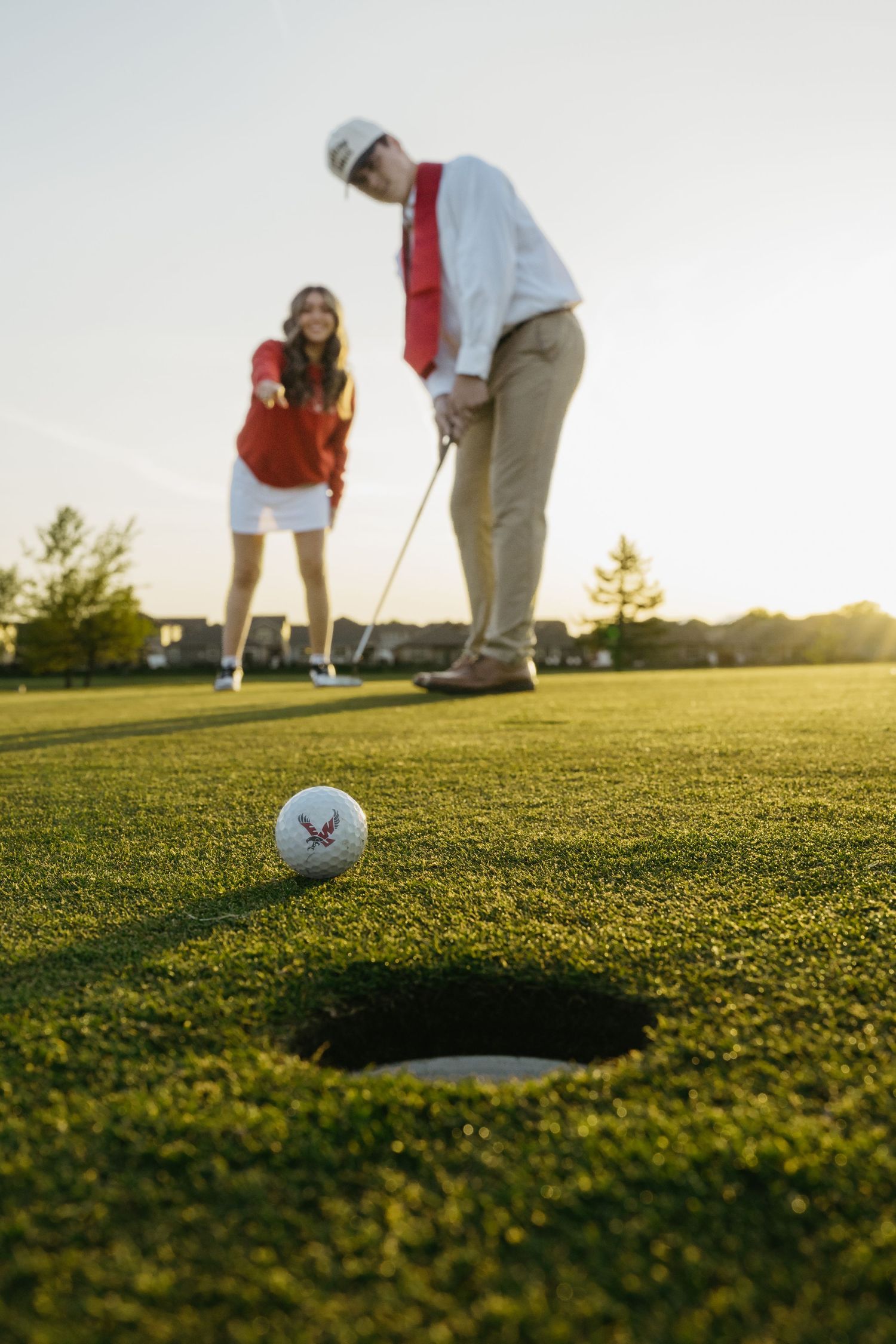 Two golfers on a sunny green watching a golf ball roll toward the hole during a golden hour putting session.