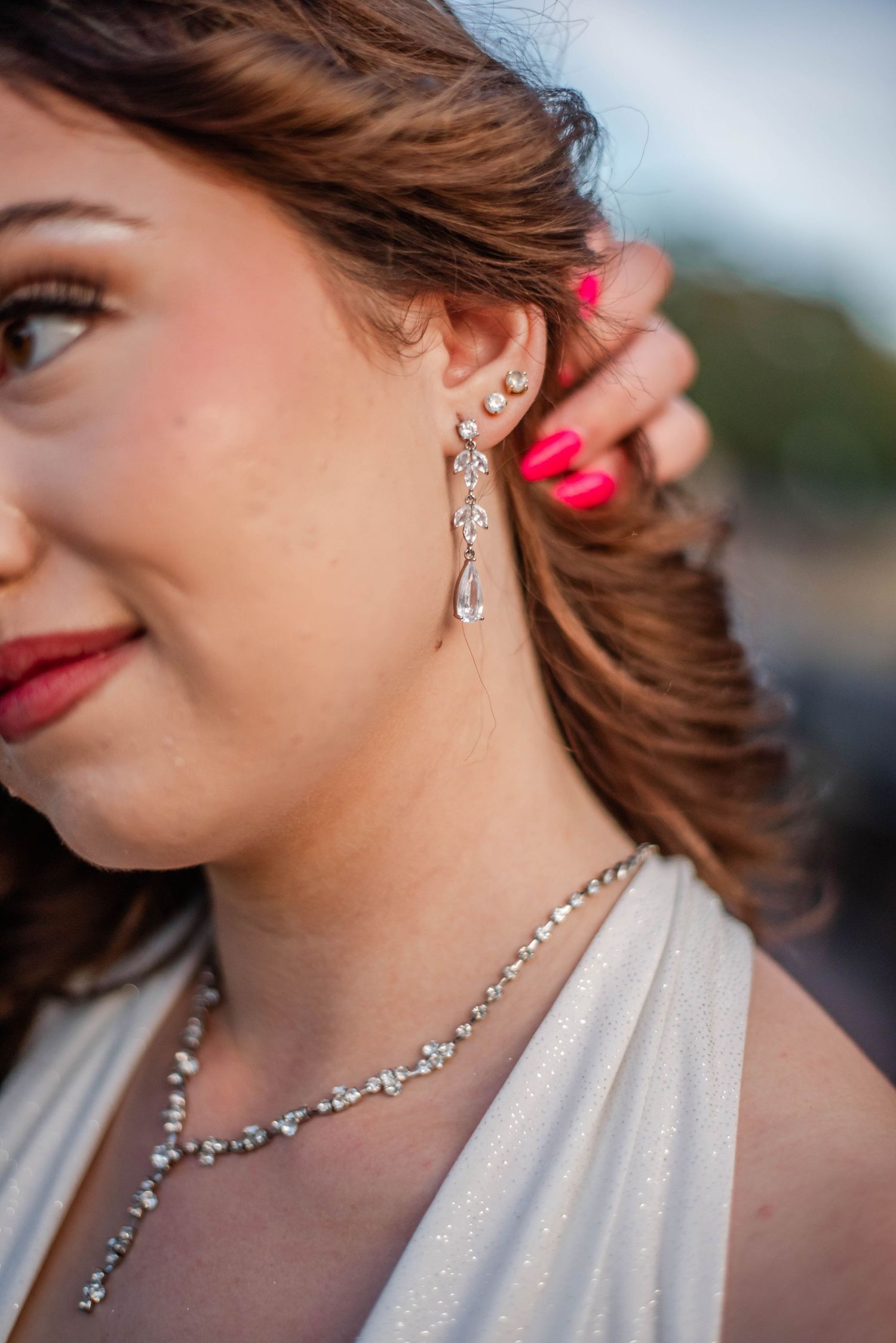 Close-up of a bride wearing elegant crystal drop earrings and a diamond necklace with red lips and pink nails.