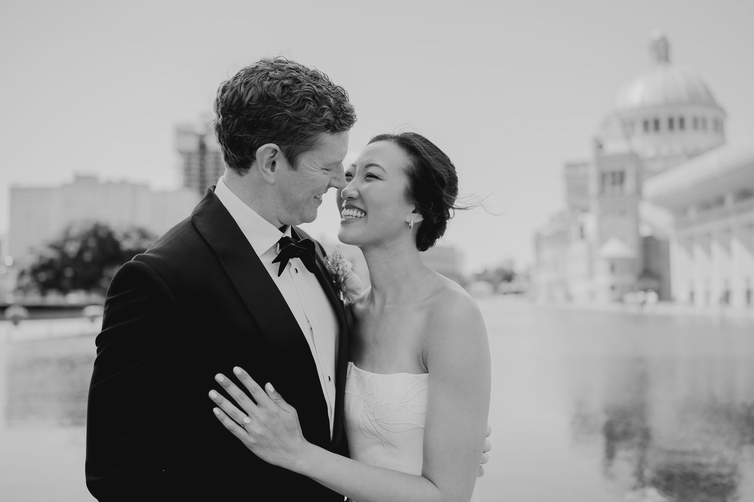 Black and white photo of a bride and groom sharing a romantic moment outdoors near a reflecting pool.