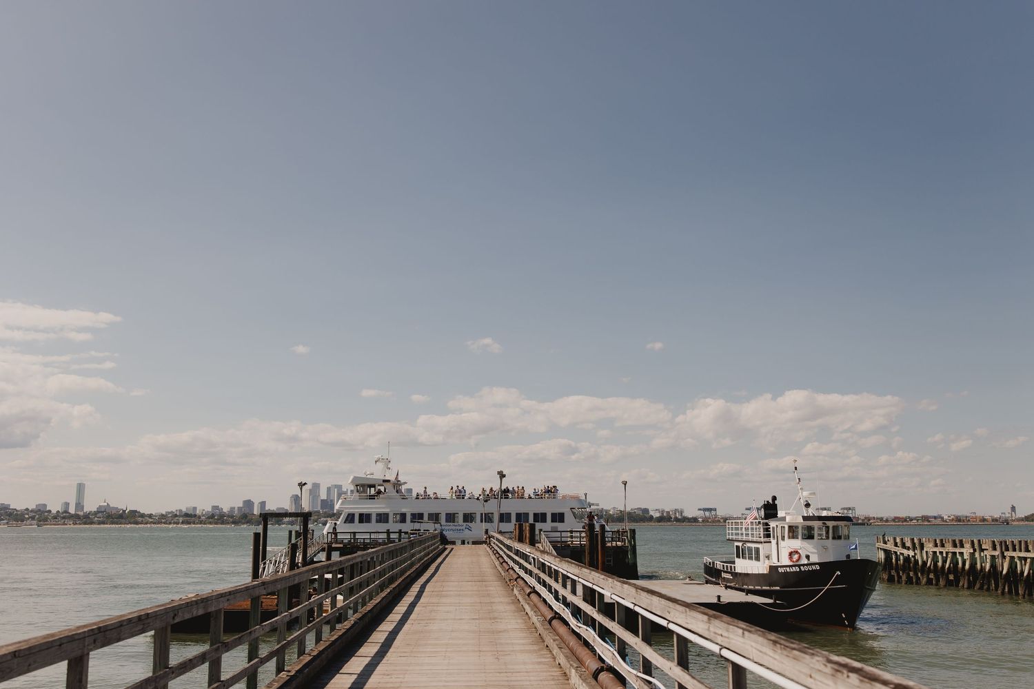 Wooden pier dock with boat moored alongside on calm blue waters under partly cloudy sky.