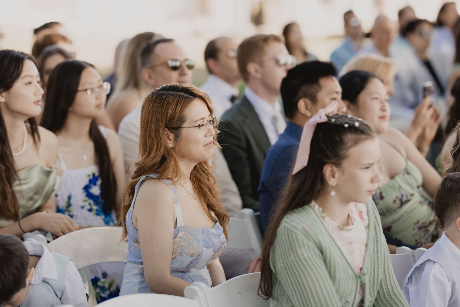 Guests seated outdoors at a wedding ceremony, featuring diverse attendees in elegant attire enjoying the celebration.