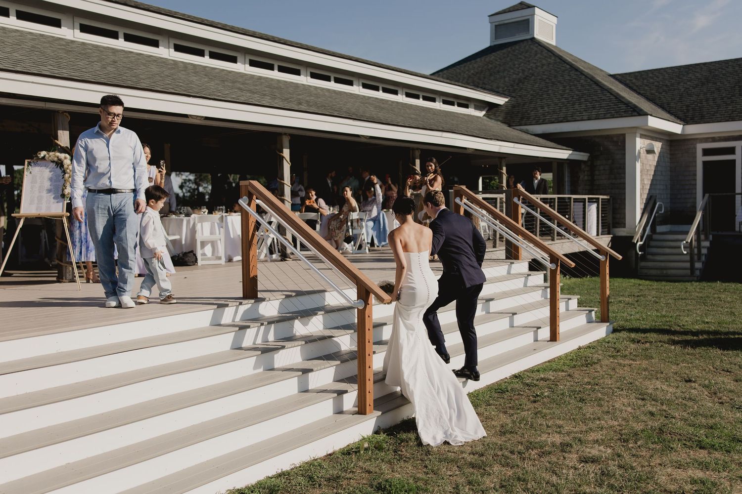 Bride and groom walk up white outdoor steps at elegant wedding venue during reception.