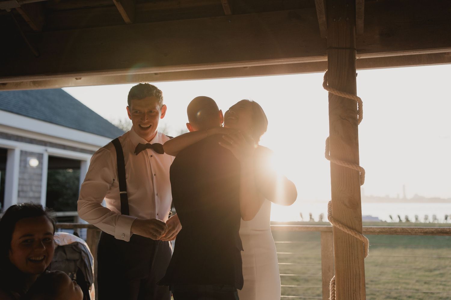 Couple sharing a romantic moment at golden hour wedding reception under rustic wooden pergola with warm sunlight.