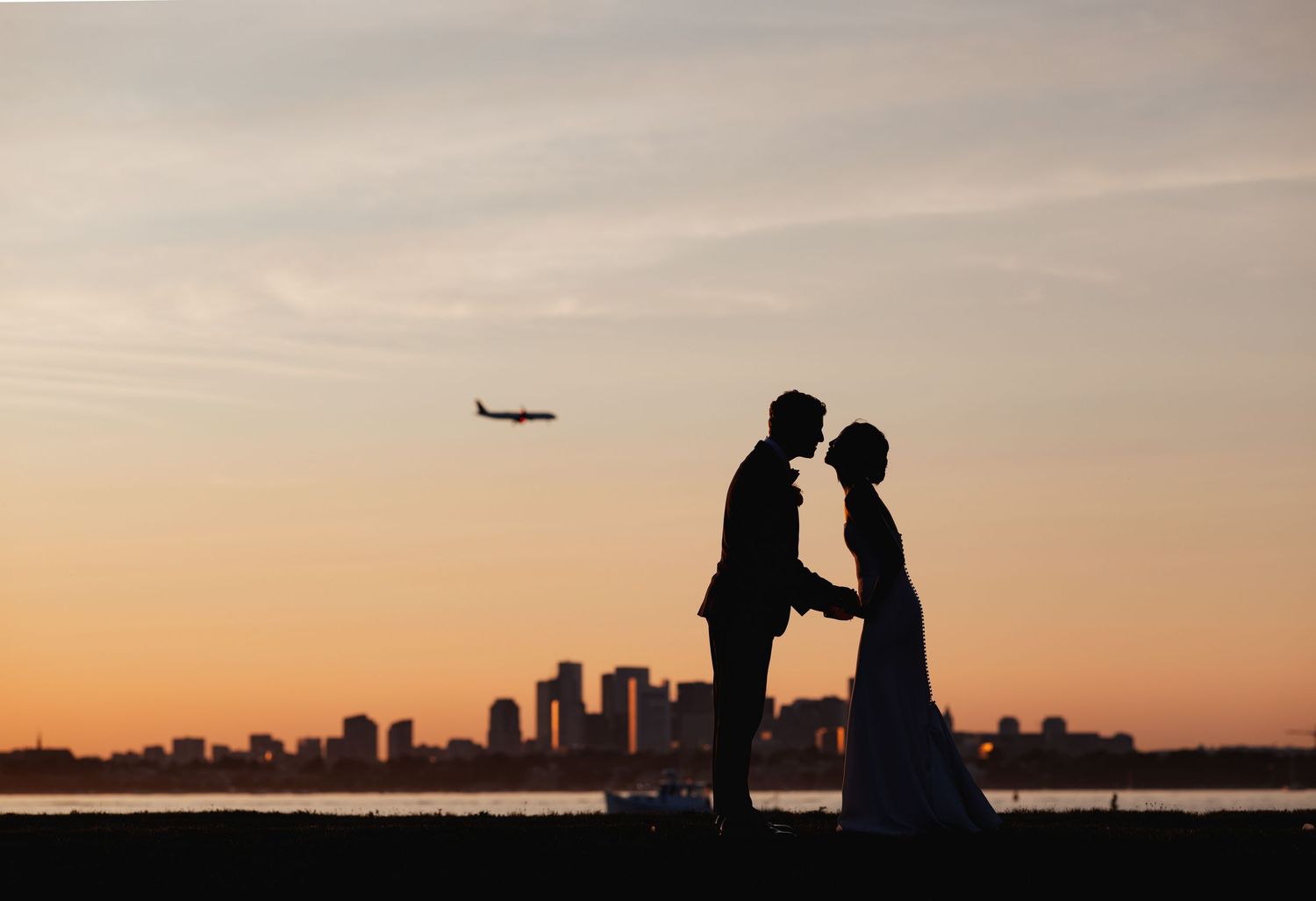 Romantic silhouette of bride and groom at sunset with city skyline and airplane in background.