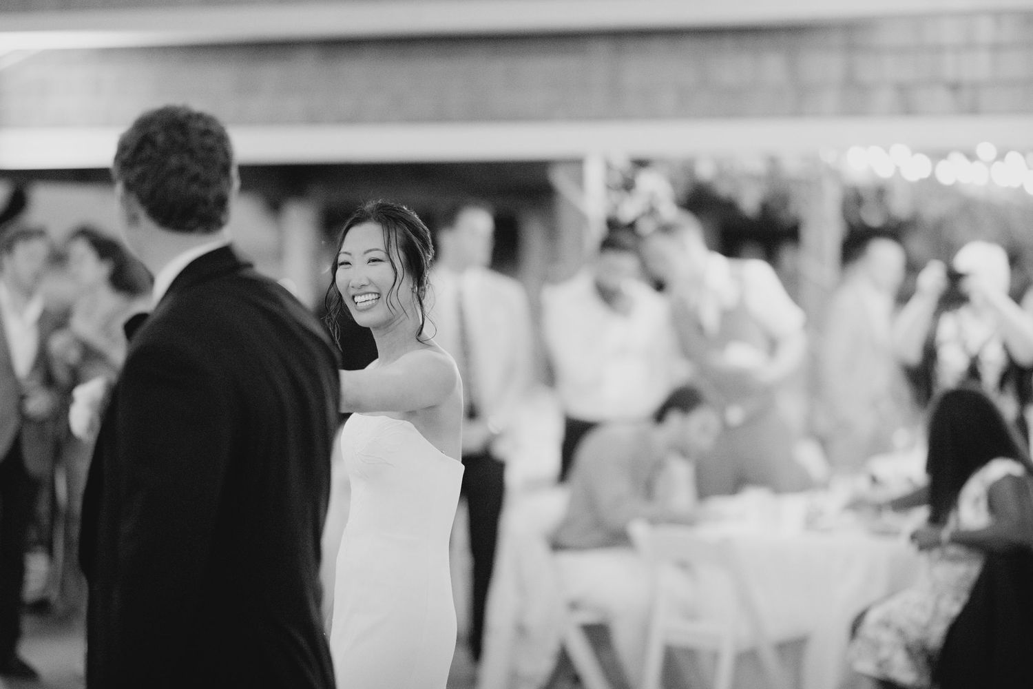 Black and white photo of a joyful bride smiling at her groom during their first dance at the reception.