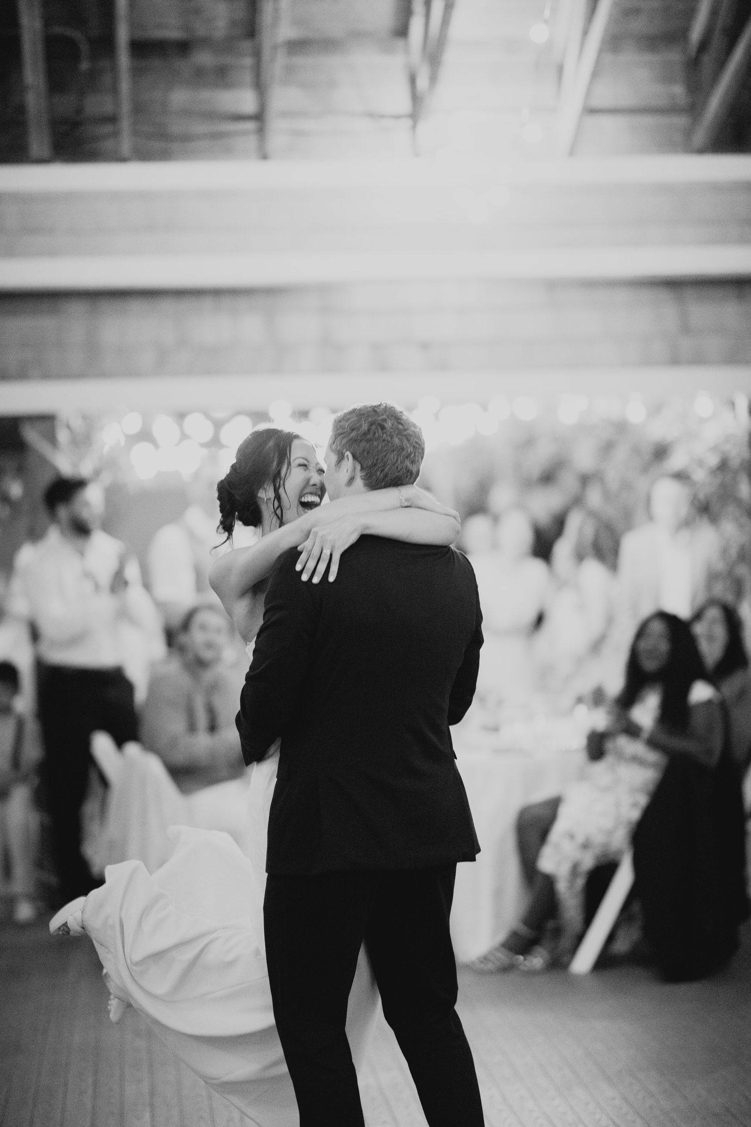 Black and white photo of groom lifting laughing bride during joyful first dance at wedding reception.