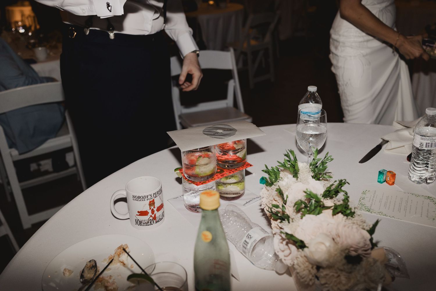 Wedding reception table with floral centerpiece, mugs, water bottles, and party favors after celebration.