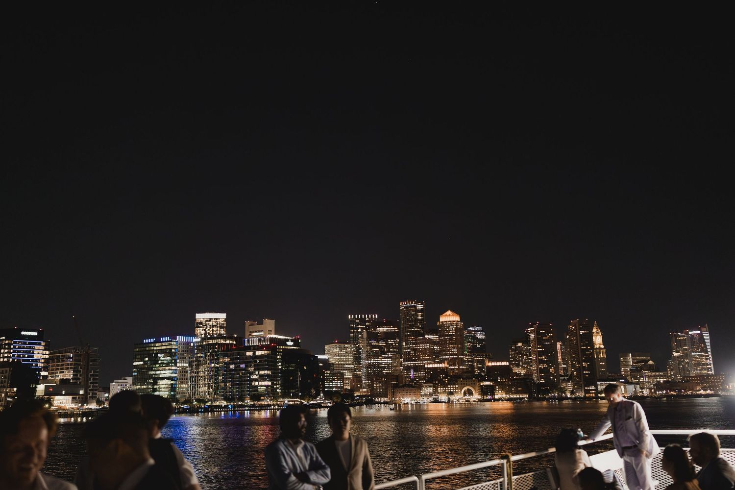 Wedding guests enjoy a stunning nighttime city skyline view from the deck of a boat.