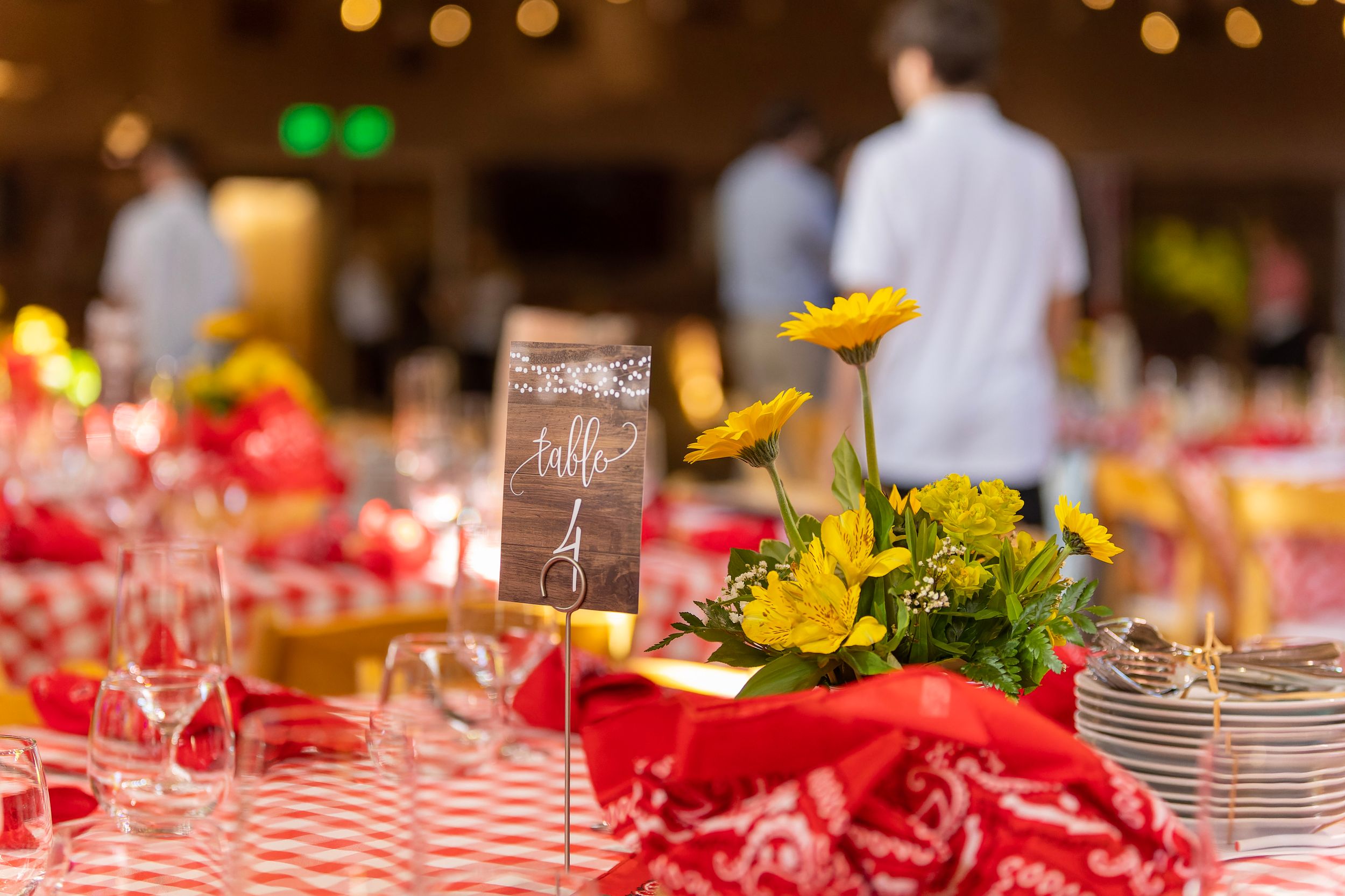Red checkered tablecloth with yellow flower centerpiece and table number sign at an elegant banquet event.