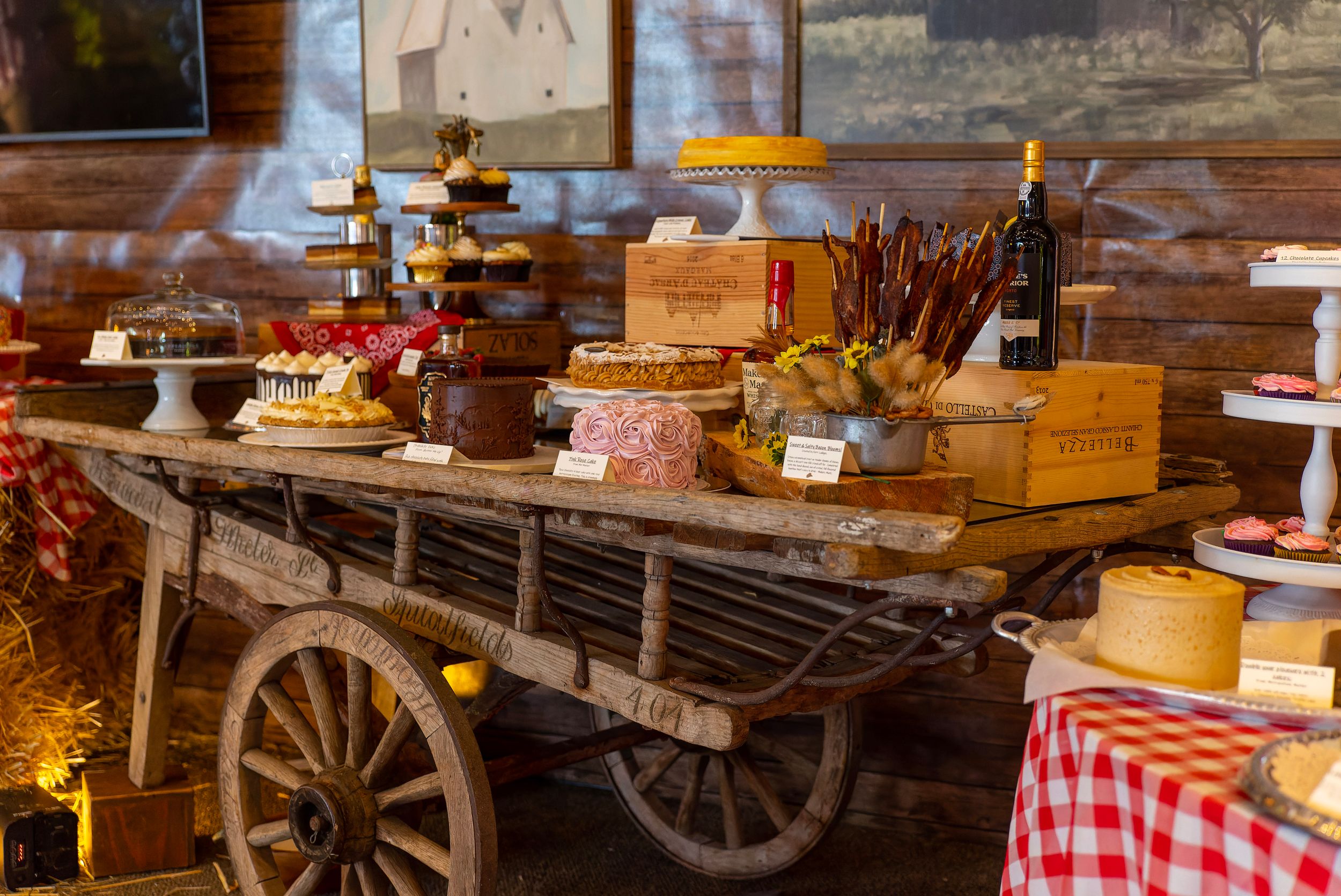 Rustic wooden cart displaying an assortment of cheeses, cured meats, and wine in a warmly lit barn setting.