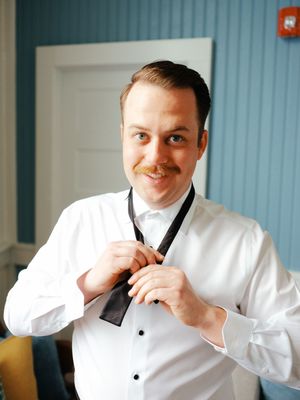 Person in formal white dress shirt and black vest adjusting their attire.