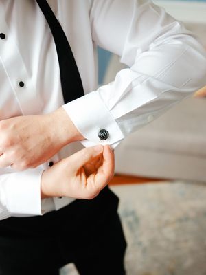 Close-up of formal white dress shirt cuffs with black buttons being adjusted.