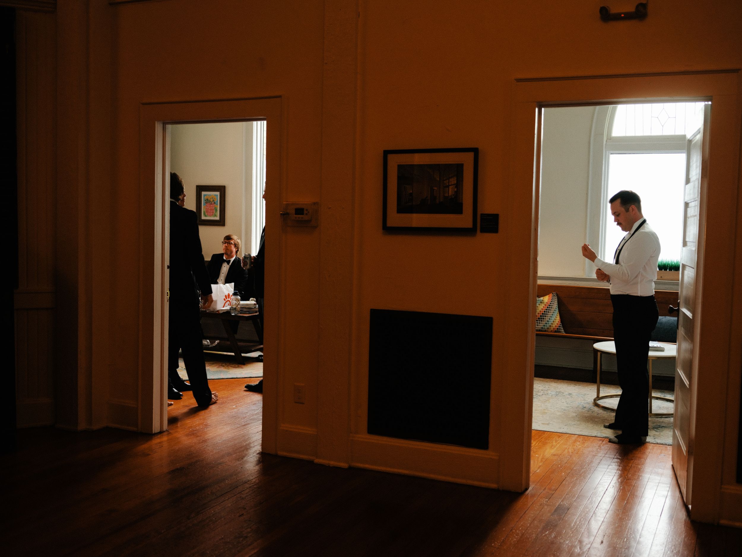 Two rooms connected by a doorway in a historic building with hardwood floors and warm lighting.