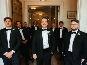 Groomsmen in black tuxedos and bow ties posing together in an elegant hallway.