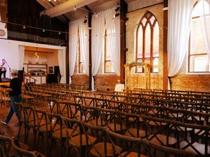 Gothic church interior with rows of wooden chairs and arched windows draped with white curtains.