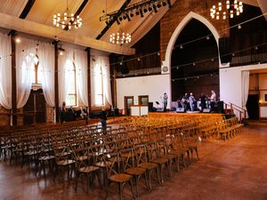 Elegant wedding venue with rustic wooden cross-back chairs and warm chandelier lighting creating an intimate atmosphere.