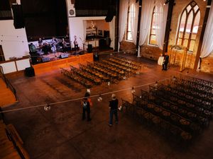Large church venue with rows of chairs set up for a wedding ceremony and gothic arched windows.