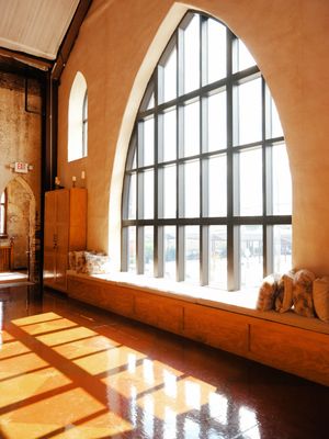 Sunlight streams through arched windows in an empty room creating dramatic shadows on the polished floor.