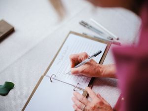 Close-up view of hands writing on paper with pen and clipboard showing detailed note-taking process.