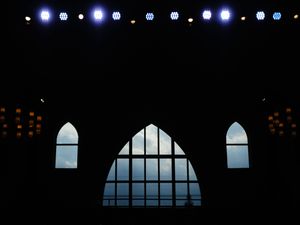 Stage lights illuminating a dark theater with arched windows silhouetted against the night sky.