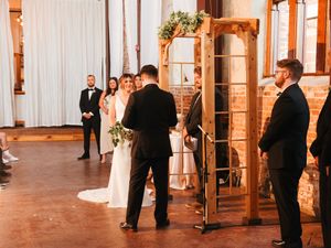 Wedding ceremony in progress inside a rustic venue with wooden pillars and white draping.