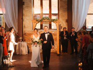 Romantic wedding ceremony in an industrial brick venue with white draping and floral decorations.