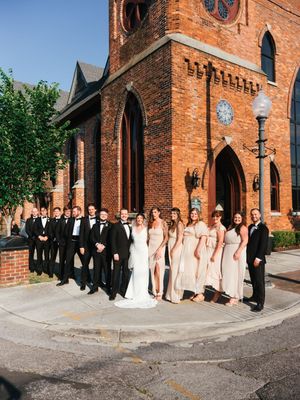 Wedding party poses outside historic red brick church with gothic architecture.