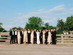 Wedding party posing for outdoor group photos against a bright blue sky and wooden fence.