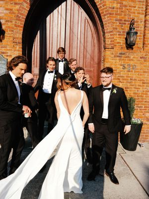 Wedding party walking outside brick archways in formal black and white attire.