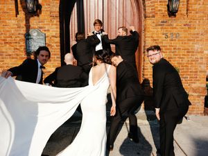 Wedding party holding white fabric against brick wall backdrop.