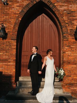 Elegant couple in formal attire standing in front of gothic church doorway.