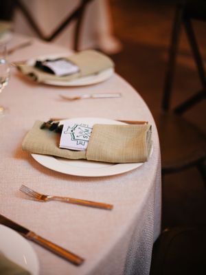 Place setting at wedding reception with beige napkin and menu card on white tablecloth.