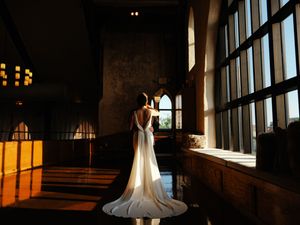 Silhouetted figures in wedding attire against large windows during golden hour.