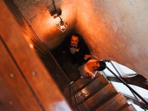 Wedding dress trailing down dimly lit vintage staircase with warm lighting.