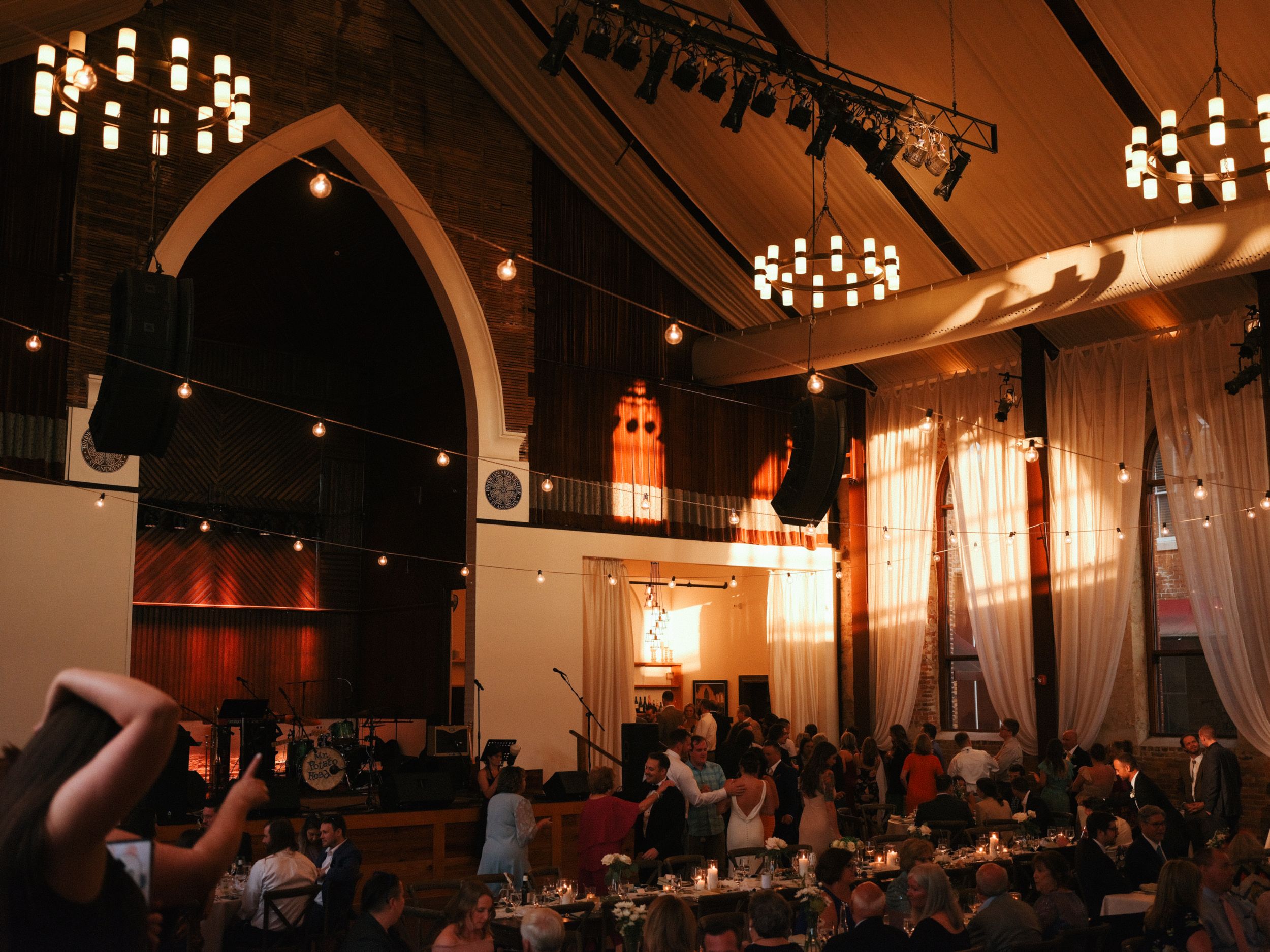Dimly lit reception hall with hanging chandeliers and string lights creating an intimate atmosphere.