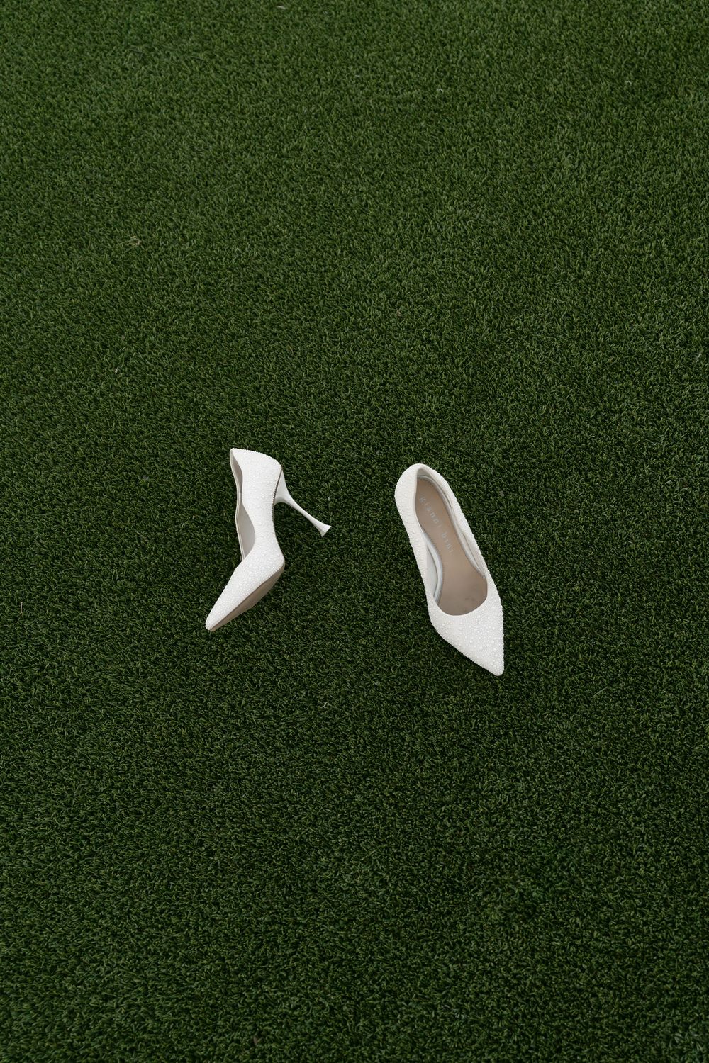 White stiletto heels placed on lush green grass, perfect for an outdoor wedding.