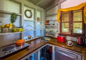 Compact rustic kitchen with wooden countertops, colorful cookware, and fresh tropical fruits on display.